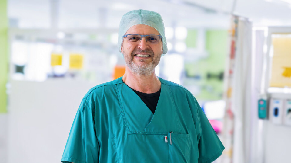 Markus Trezeciak, Leitung Herz-Thorax-Gefäßchirurgischer OP Ein lächelnder Arzt mit Brille in einem grünen OP-Kittel